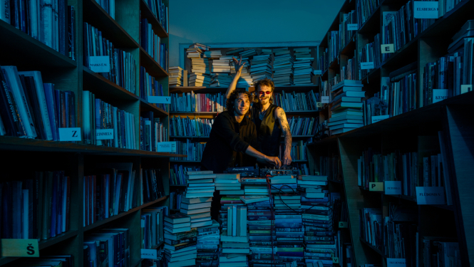 Divi dīdžeji bibliotēkā starp grāmatu plauktiem