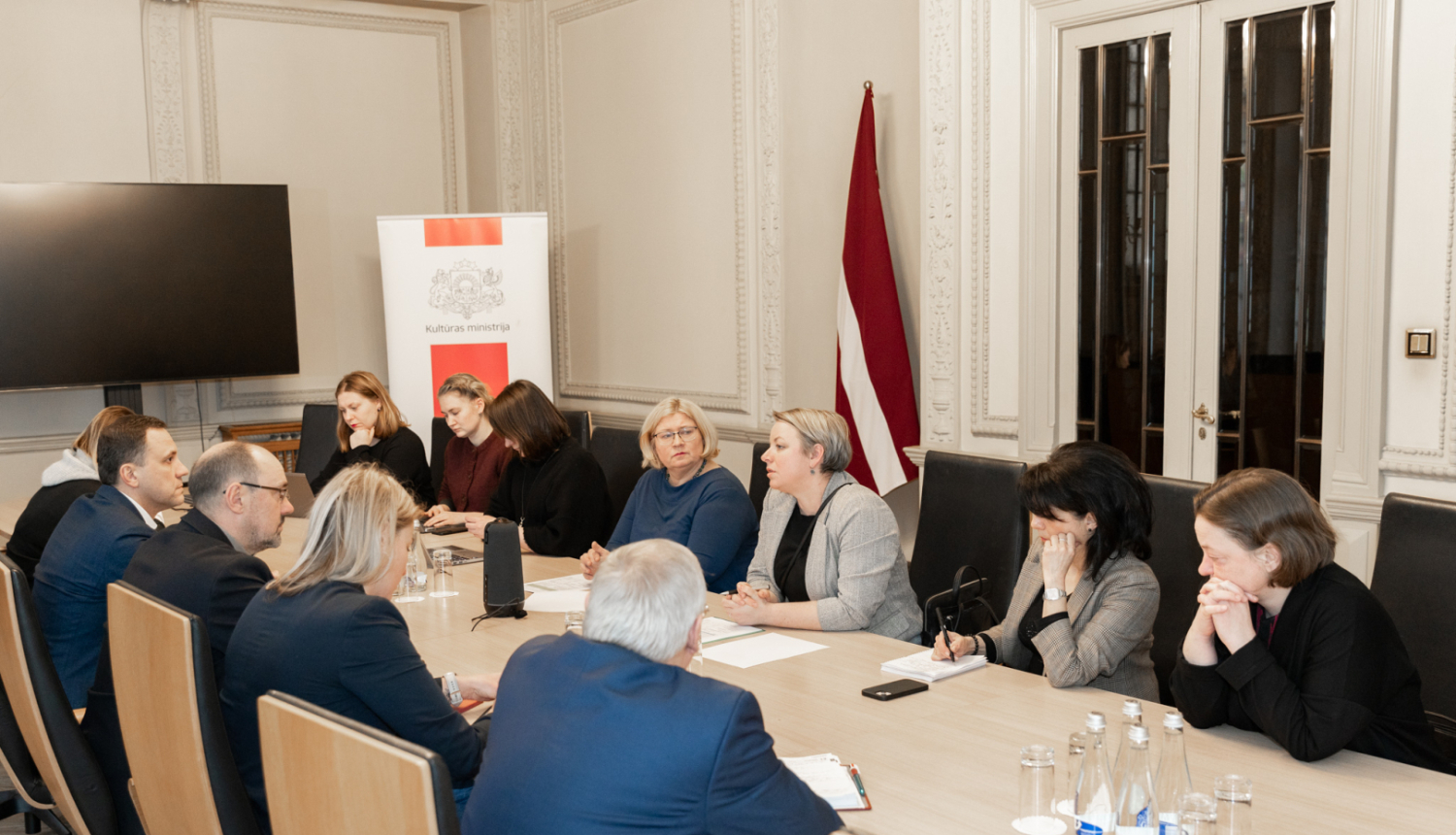Vienpadsmit cilvēki pie sanāksmju galda
