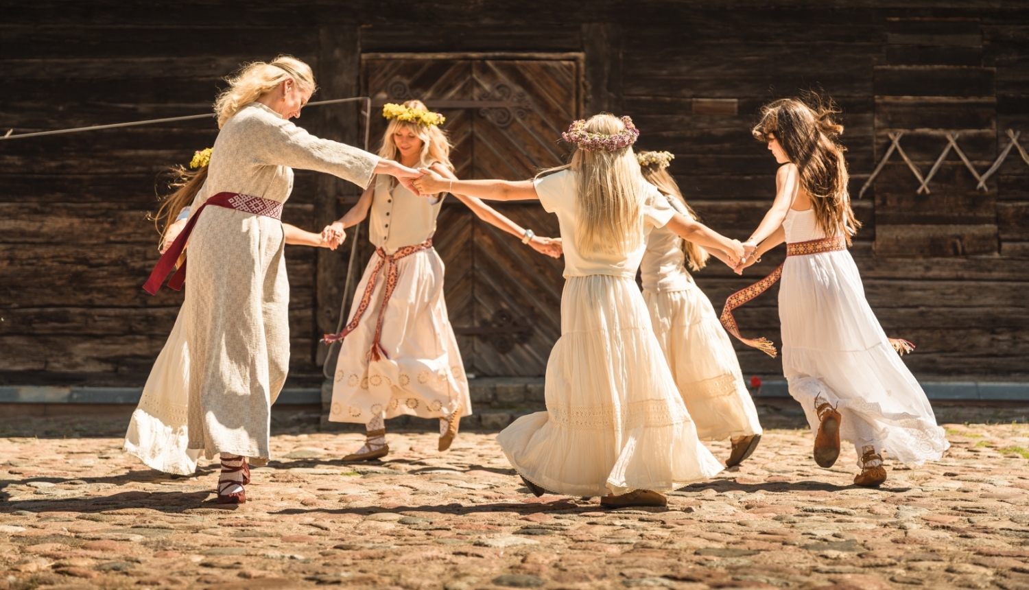 Piecās dejotājas tautiskos tērpos griež danci pagalmā