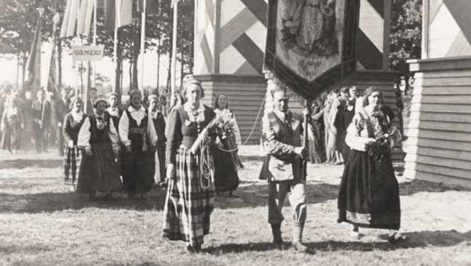 Melnbalta sena fotogrāfija, kurā redzami Dziesmu un deju svētku dalībnieki