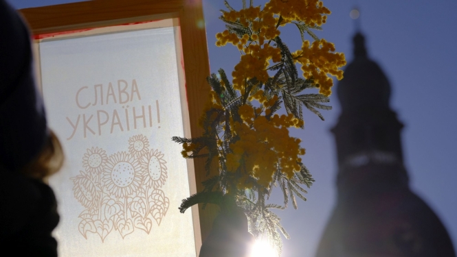 Sietspiedes tehnikā darināts ornaments un dzelteni ziedi uz debesu fona