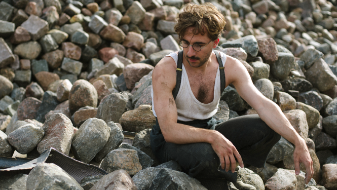 Kadrs no filmas materiāla: filmas varonis sēž akmeņainā jūras krastā