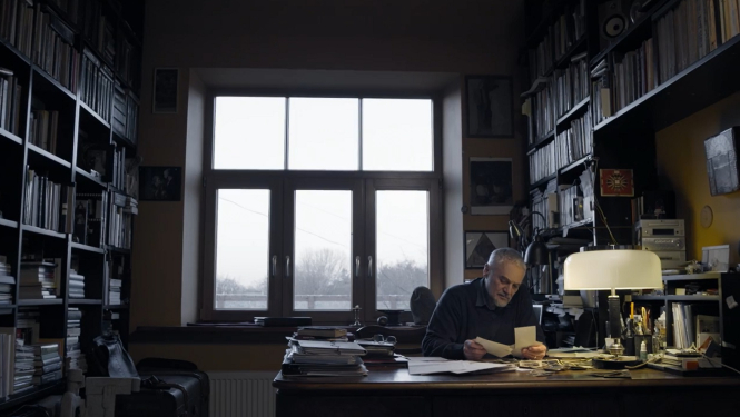 Kadrs no filmas "Uz spēles Latvija" (2014), režisors Pēteris Krilovs sēž istabā pie galda
