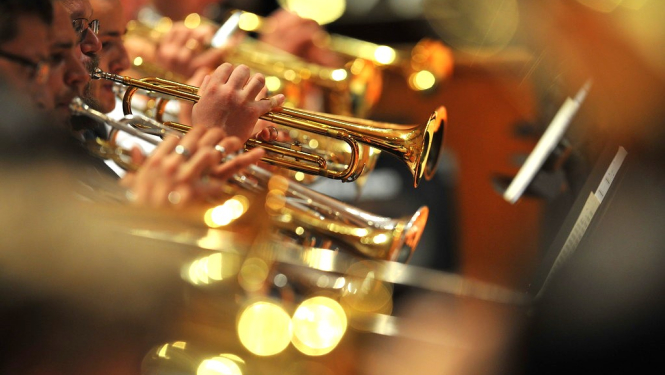 Orķestra dalībnieki pūšaminstrumentu grupā spēlē koncertā