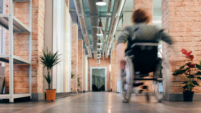 Persona ar invaliditāti ratiņkrēslā, pārvietojoties pa gaiteni