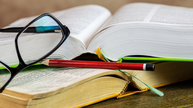 Uz divām atvērtām grāmatām novietots zīmulis un brilles.
