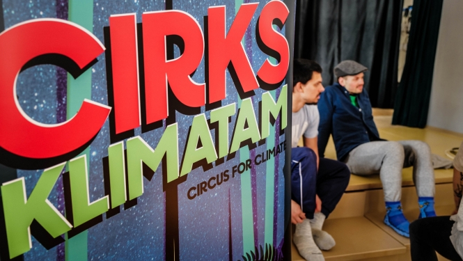 Uzraksts: Cirks klimatam. Divi sēdoši skatītāji.