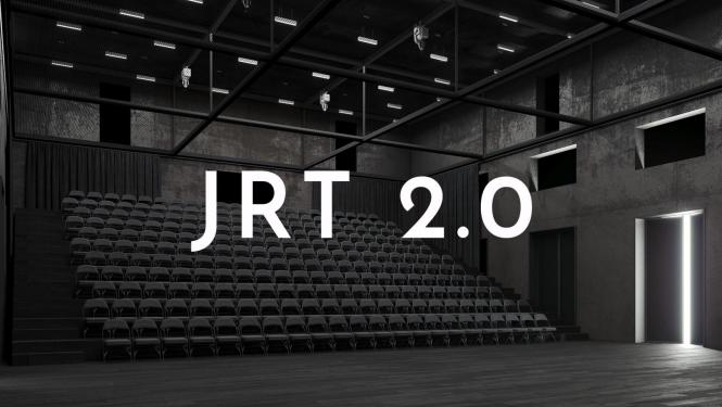 Balts uzraksts "JRT 2.0", fonā skatītāju vietas Jaunā Rīgas teātra pagaidu telpās Tabakas fabrikā
