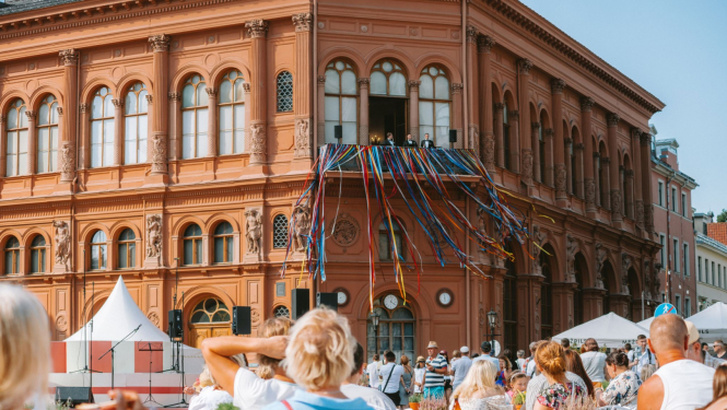 Mākslas muzeja Rīgas Birža fasāde skatā no Doma laukuma, priekšplānā cilvēki sēž