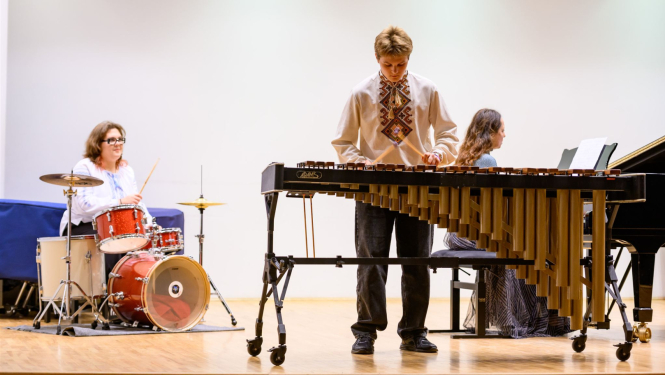 Divi mūziķi uz skatuves; viens pie bungām, otrs pie marimbas