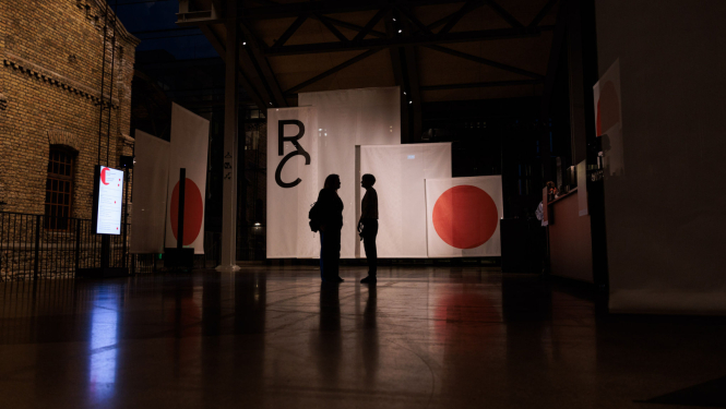 Riga Contemporary atklāšanas vakarā izstāde Hanzas peronā, uz baneru fona divu cilvēku figūras. Foto: Ģirts Raģelis