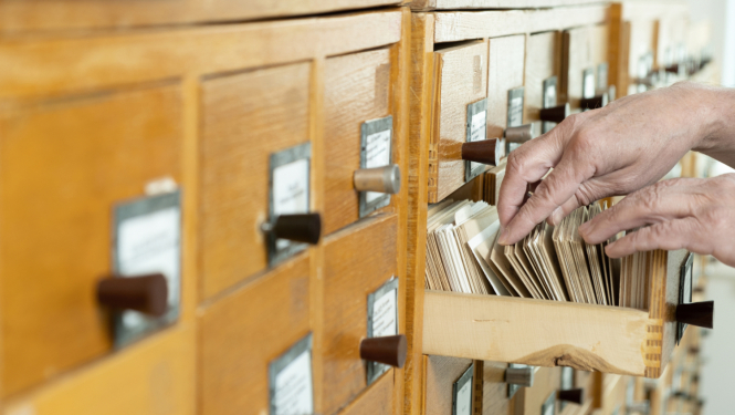 Cilvēks pāršķirsta arhīva kartītes vienā no arhīva skapja atvilknēm