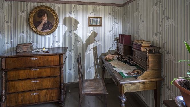 Ekspozīcija Raiņa un Aspazijas mājā Rīgā - istaba, rakstāmgalds, kumode un Aspazijas ēnas siluets, kas projecēts uz sienas