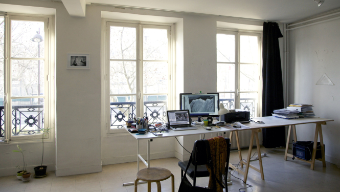 Cite Internationale des Arts gaiša darba vieta ar logiem. Uz galda datori, kancelejas piederumi