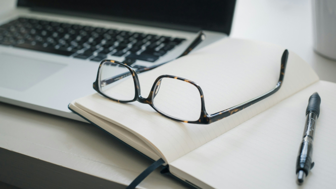 Dators, brilles un piezīmju blociņš uz galda