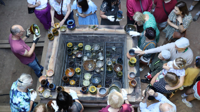 Cilvēki apkārt glazētiem keramikas traukiem, kas tiek ņemti ārā no cepļa