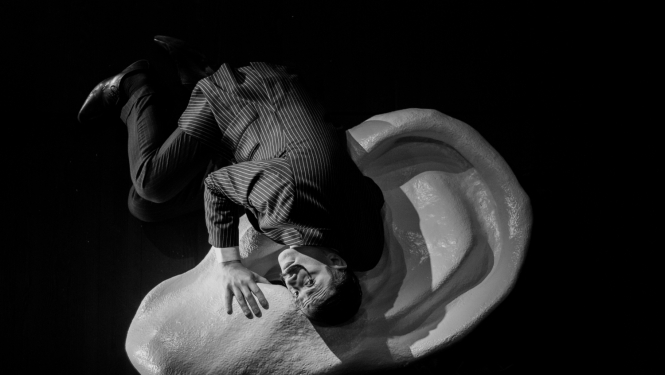 Melnbalts attēls - aktieris guļ uz lielas auss figūras