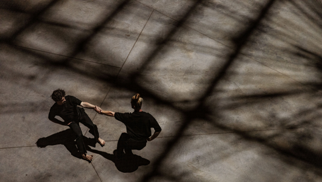 Divi cilvēki noēnotā telpā dejo tukša laukuma vidū