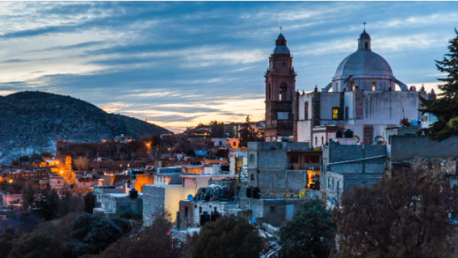 Pilsētas ainava naksnīgā apgaismojumā, fonā kalni