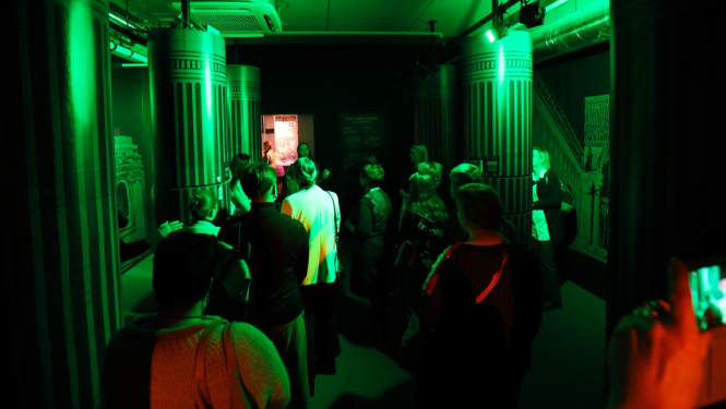 Cilvēki klausās izziņu centra zaļi apgaismotā telpā