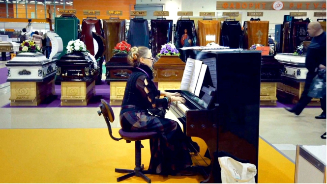 Kadrs no Dāvja Sīmaņa dokumentālās filmas „Frankenšteins 2.0” - sieviete sēž pie klavierēm apbedīšanas biroja telpās