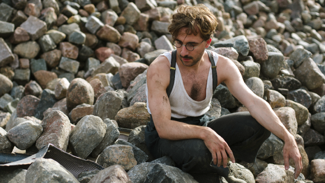 Kadrs no filmas materiāla: filmas varonis sēž akmeņainā jūras krastā