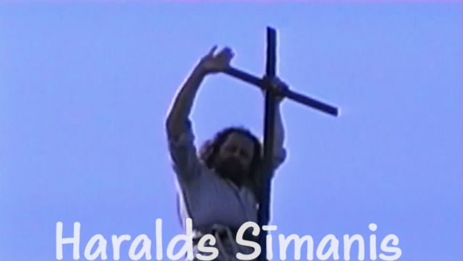 Filmas kadrs ar mūziķi Haraldu Sīmani un koka krustu. Teksts: Haralds Sīmanis, dziesminieks un jumiķis