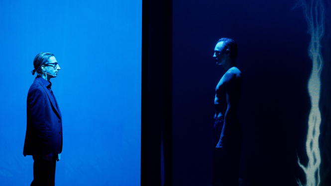 Daugavpils teātra izrādes “Kaids nūteikti atīs” (“Kāds noteikti atnāks”) aktieru silueti uz skatuves zilas krāsas apgaismojumā