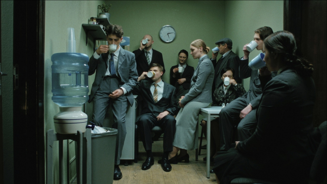 Kadrs no filmas - cilvēku grupa uzvalkos ofisa virtuves telpā