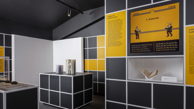 Latvijas Nacionālās bibliotēkas izstādes ekspozīcija, paneļi tumši pelēkā un dzeltenā krāsā, izstādes eksponāto