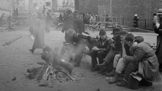 Kadrs no filmu materiāla. Cilvēki sēž pie ugunskura barikāžu laikā.
