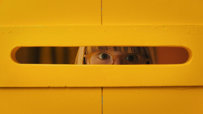 Kadrs no filmas materiāla: meitene bailīgi skatās caur spraugu