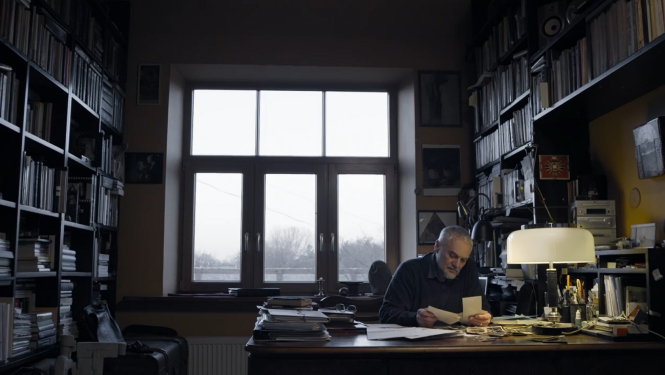 Kadrs no filmas "Uz spēles Latvija" (2014), režisors Pēteris Krilovs sēž istabā pie galda