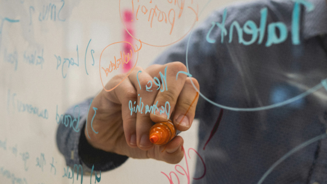 Cilvēks raksta ar marķieri uz caurspīdīgas/stikla tāfeles virsmas