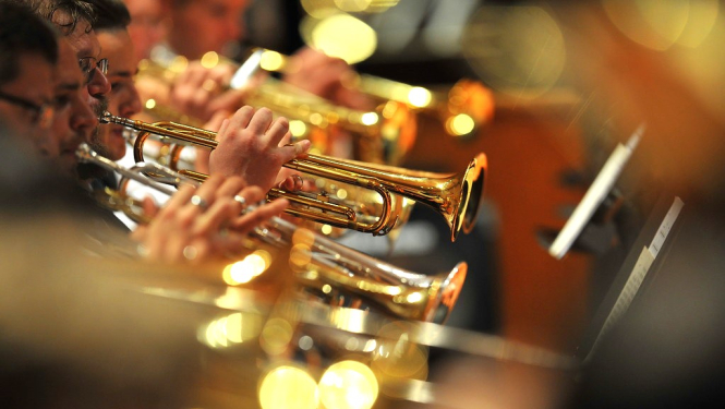 Orķestra dalībnieki pūšaminstrumentu grupā spēlē koncertā
