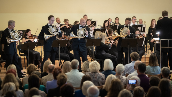 Skatītāji klausās kā uz skatuves Liepājas Simfoniskais orķestris koncertē