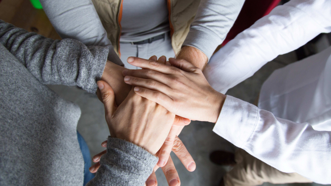 Trīs cilvēku rokas saliktas viena uz otras tikšanās laikā