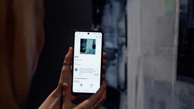 Rokas ar tālruni, kurā atvērta Rotko muzeja mobilā lietotne