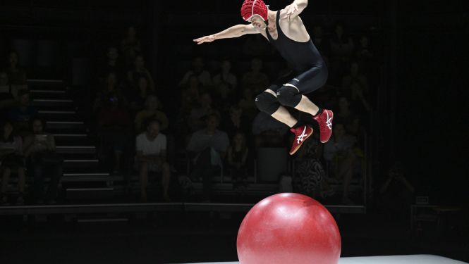 Cirka akrobāts arēnā izpilda vingrojumu uz sarkanas bumbas