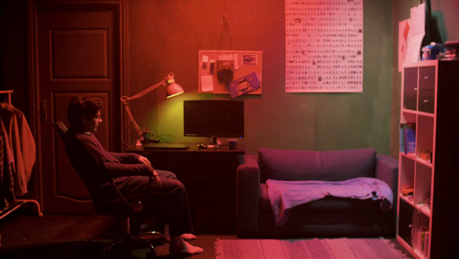 Kadrs no LKA un Latvijas Kultūras koledžas studentu filmas, cilvēks vāji agaismotā telpā sarkanā apgaismojumā