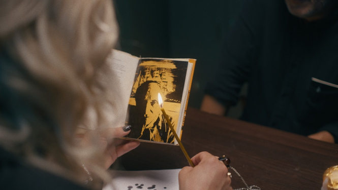 Kadrs no režisora Jāņa Ābeles dokumentālās filma “Testaments”, kadrā cilvēks, kas tur rokā grāmatiņu un sveci