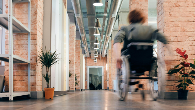 Persona ar invaliditāti ratiņkrēslā, pārvietojoties pa gaiteni