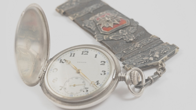 Pulksteņa breloks ar Latvijas Aizsargu organizācijas simboliku, piekārts pie kabatas pulksteņa “Zenith”.