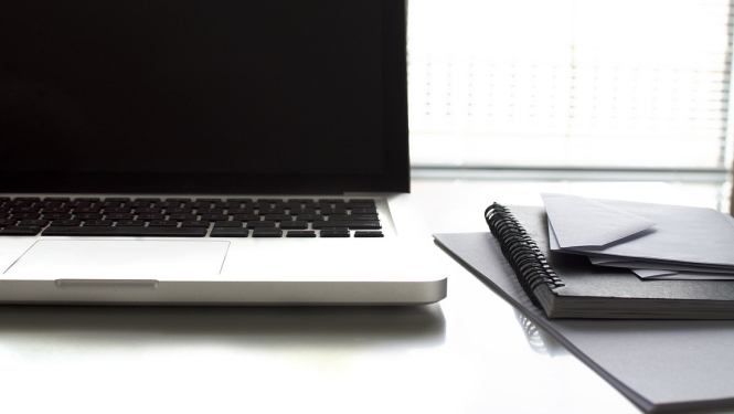 Dators un piezīmju blociņš uz galda.