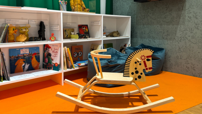 Izstādes iekārtojums plaukti ar bērnu grāmatām, rotaļlietām un koka šupuļzirdziņš