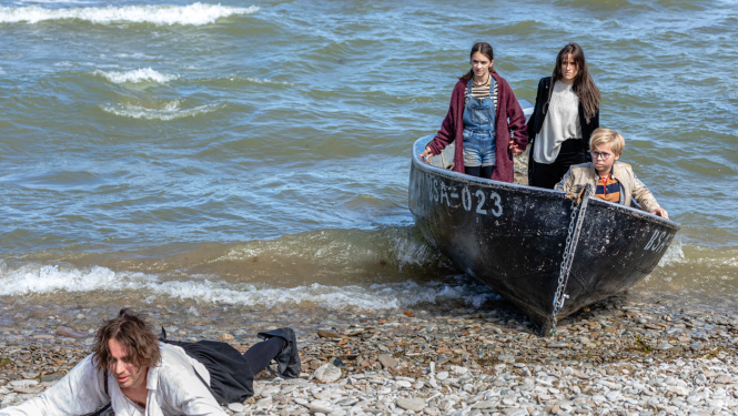 Filmas kadrs: trīs bērni laivā un vīrietis krastā