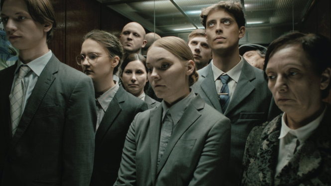 Kadrs no īsmetrāžas filmas “Kur saulīte nakti guļ?” - kadrā cilvēku grupa liftā