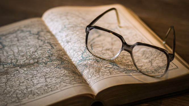 Smalka karte atvērta grāmatā, uz tās novietotas brilles.