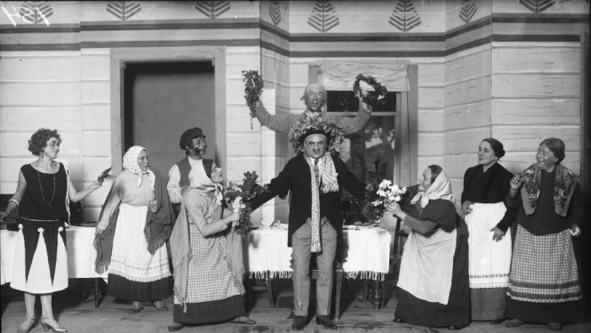 Aina no A. Saulīša komēdijas “Inteliģenti” uzveduma Nacionālā teātra aktieru izpildījumā. No kreisās: 1. Anta Klints - Adelīnas lomā, 6. Alfrēds Amtmanis-Briedītis - Fēliksa Šmigas lomā, 8. Berta Rūmniece - Vēsmiņas mātes lomā, 9. Ella Jēkobsone - Salmienes lomā. Rīga, 1925.gads. Autors nav zināms. Latvijas Valsts kinofotofonodokumentu arhīvs, LNA_KFFDA_F1_9_154