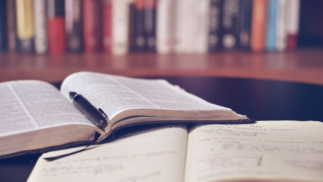 Atverta grāmata un pierakstu klade uz galda bibliotēkā